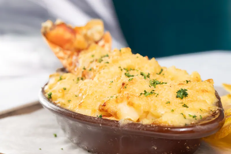 Baked lobster macaroni and cheese in an oval dish, browned on top and finished with chopped parsley, on marble